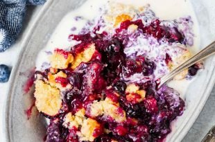 A photo of a serving of blueberry cobbler in a bowl with a side of melted vanilla ice cream.