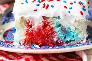 A piece of red, white and blue poke cake on a blue and white dessert plate. The cake is frosted with white frosting and sprinkled with red, white and blue sprinkles. You can see the red, white and blue portions of the cake where holes have been poked and jello poured in.