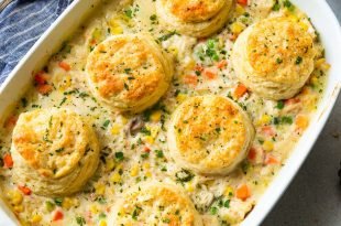 a photo of a white rectangular baking dish full of creamy chicken pot pie filling with six golden butter milk biscuits on top.