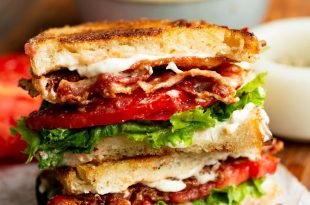 a photo of a perfect BLT sandwich with golden toasted bread, slices of crispy bacon, tomato slices and lettuce with mayo slightly seeping out the sides.