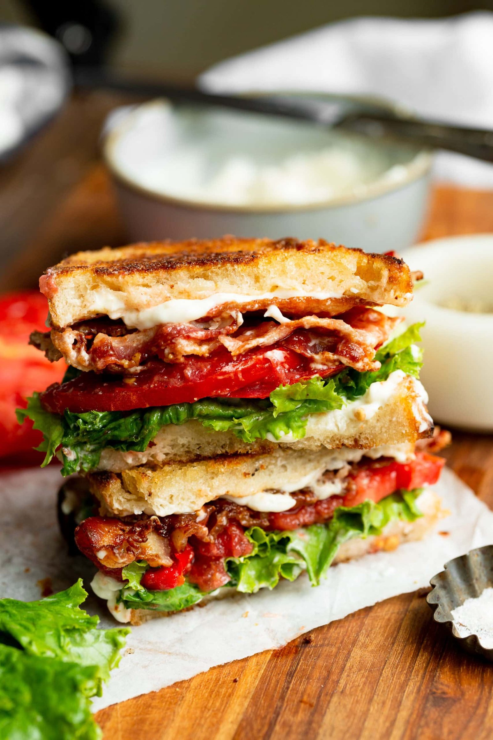 a photo of a perfect BLT sandwich with golden toasted bread, slices of crispy bacon, tomato slices and lettuce with mayo slightly seeping out the sides.