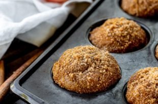 a photo of the corner of a muffin tin with baked apple cider donut muffins in it that are topped with brown sugar cinnamon.