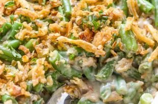 a cooked green bean casserole recipe in a white serving dish with a spoon