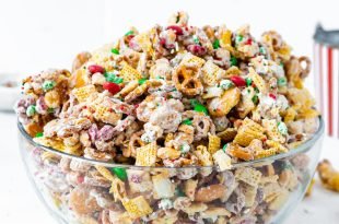 A bowl of Christmas white chocolate trash chex mix. The mix has two kinds of chex cereal, pretzels, peanuts, vanilla wafers, and m&m candies. It is covered with melted white chocolate.