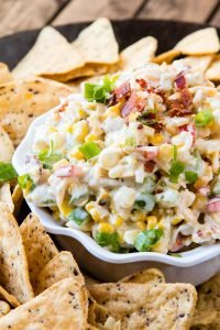 close up of corn and bacon ranch dip in white dish with tortilla chips